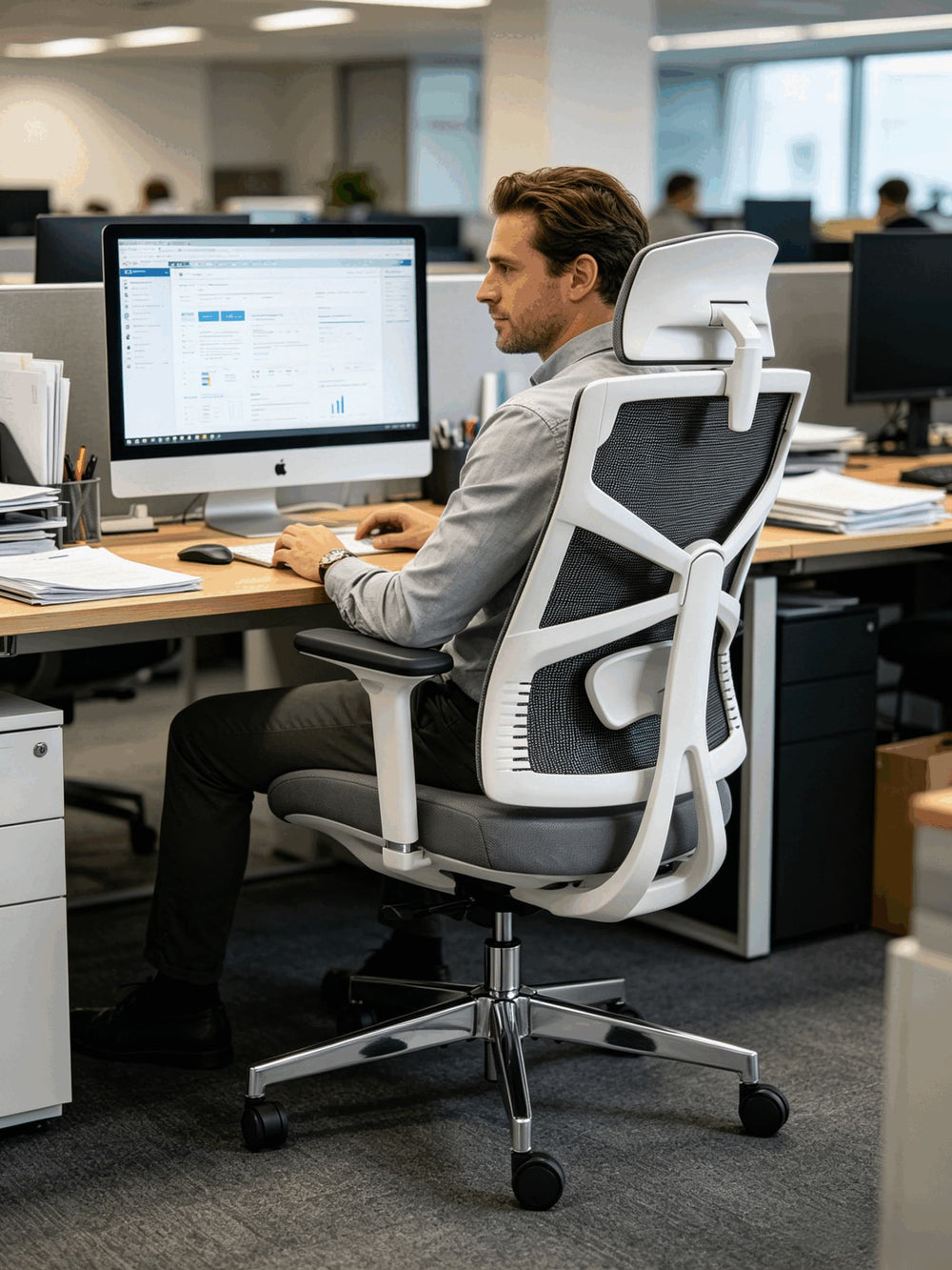Professional working at iMac in corporate office seated in HOLLUDLE Shaper white ergonomic chair showing adaptive backrest structure